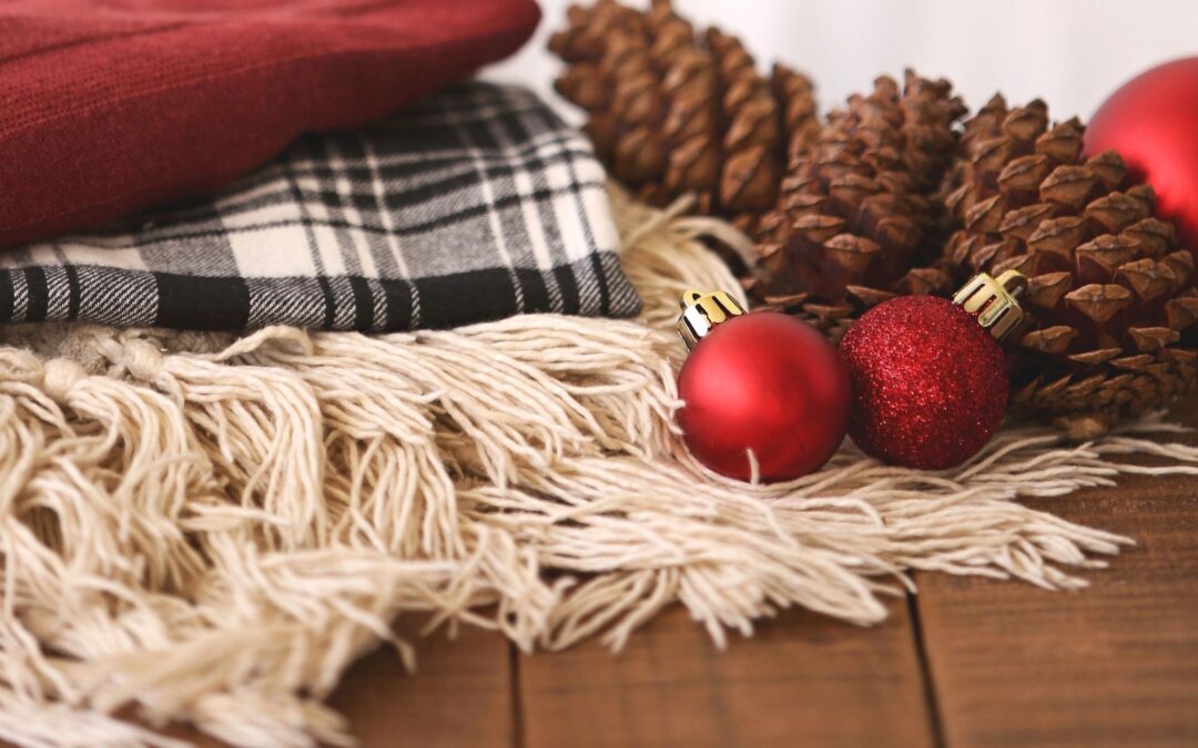 holiday season image with a wooden table and a plaid black and white blanket with red ornaments and pinecones