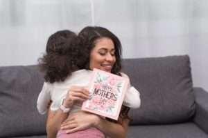 small child hugging her mom after gifting her a mother's day card, mothers day gift idea, daughter hugging her mom