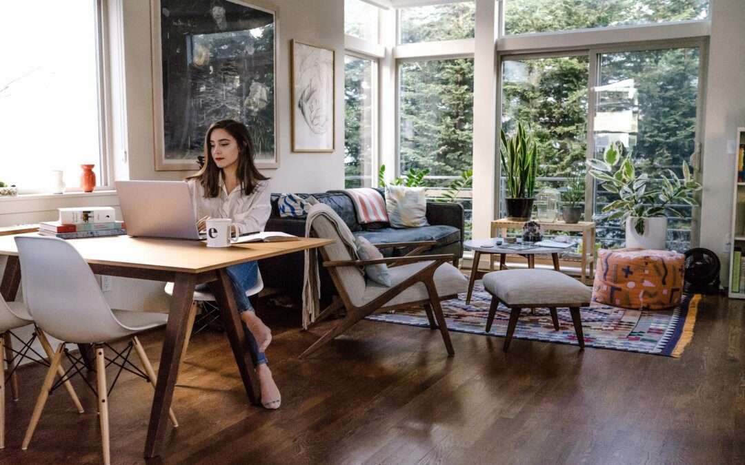 homeowner sitting at a desk/table with her laptop next to a living space with large windows