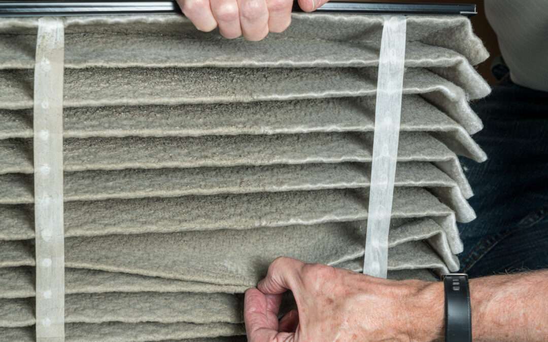 Senior caucasian man performing a winter maintenance task of changing the air filter; he is looking at the dust in folded dirty air filter in the HVAC furnace system in basement of home
