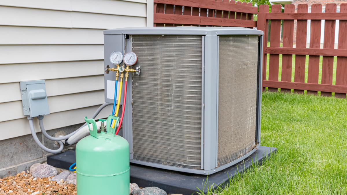 dirty air conditioning system with a layer of cottonwood outside a residential home with gauges attached and a visible refrigerant tank next to the hvac unit